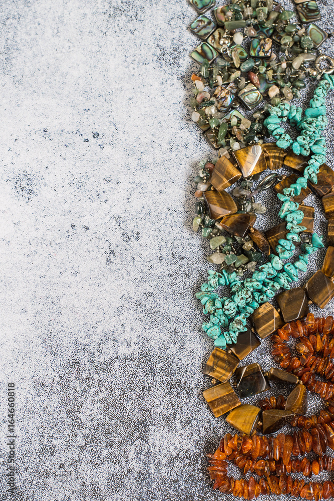  Accessories. Necklaces of various natural stones, such as jasper, turquoise, amber, tiger's eye on a gray background.