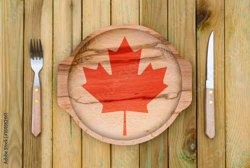 Concept of Canadian cuisine. Wooden plate with a Canada flag, fork and knife on a wooden background