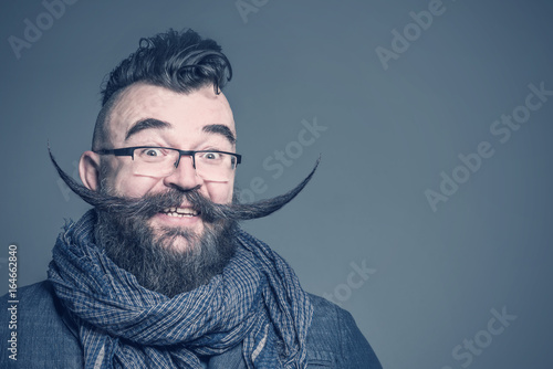 Smiling bearded man with a mohawk hairstyle and a very long mustache on a gray b Fototapet