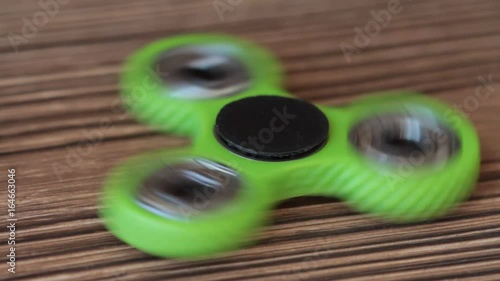 One green fidget spinner is spinning on brown wooden background. Popular relaxing toy. Selective focus. photo