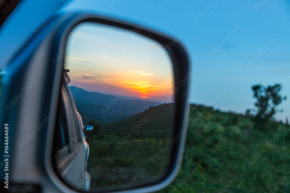 Sunset is reflected in the car's rear-view mirror