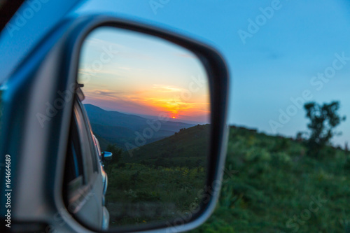 Sunset is reflected in the car's rear-view mirror