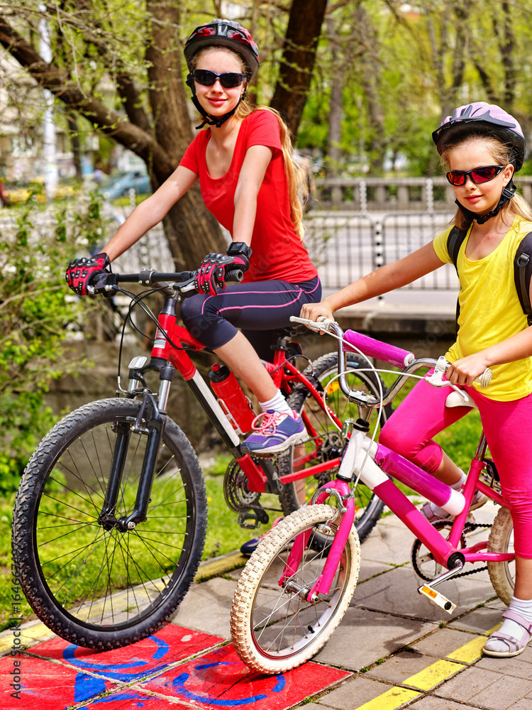 Fototapeta premium Family bike ride. Mother and daughter wearing bicycle helmet with rucksack . Children biking on yellow bike lane. Bike share program save money and time. Friendship between children of different ages.