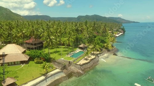Aerial view of ocean shore with villas on beach, palm trees jungles and hills in Candidasa, Bali on a sunny summer day with blue sky, flying to the right photo