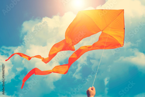 Orange kite in hand in sunny blue sky with clouds photo