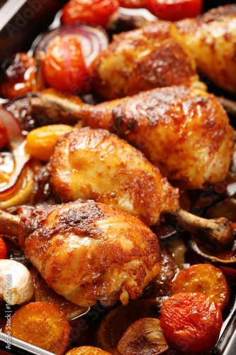 Roasted chicken legs with vegetables on wooden background