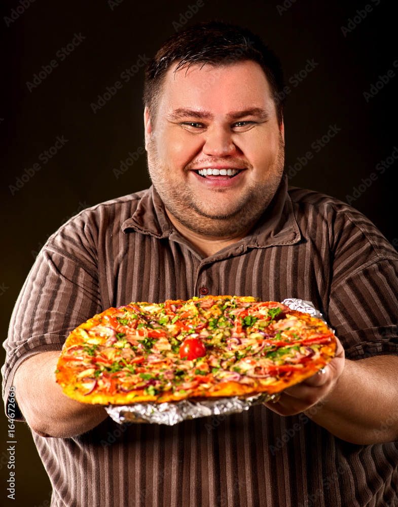 Fat man eating fast food and offers great pizza to customers and friends. Breakfast for overweight person. leads to obesity. Person regularly overeats concept on dark background. Fat man eating fast food and offers great pizza to customers and friends. Breakfast for overweight person. leads to obesity. Person regularly overeats concept on dark background.
