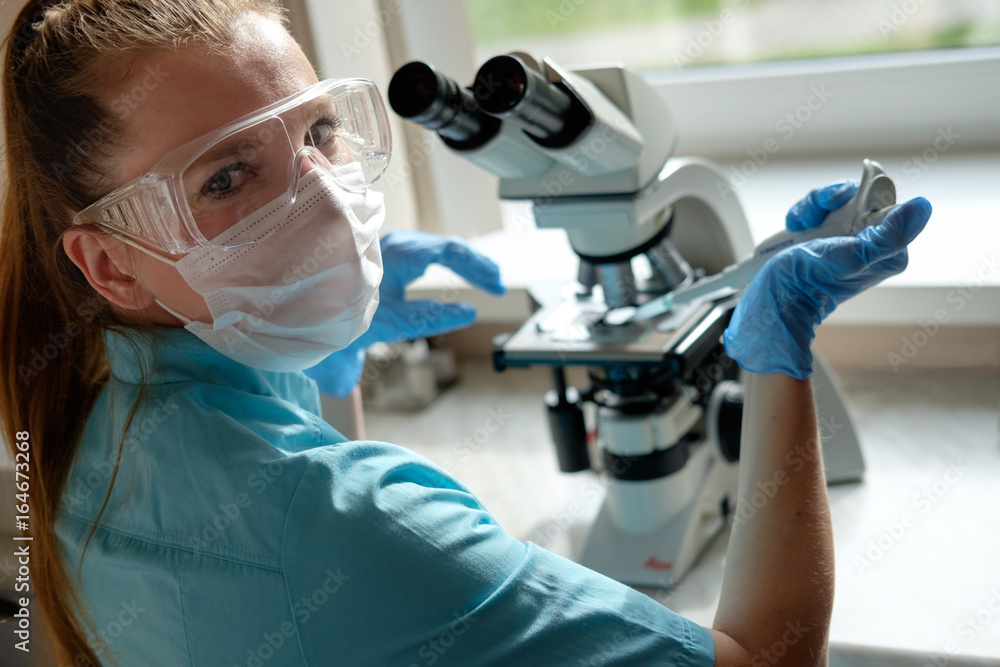 woman laborant working with microscope holding automatic pipette woman laborant working with microscope holding automatic pipette