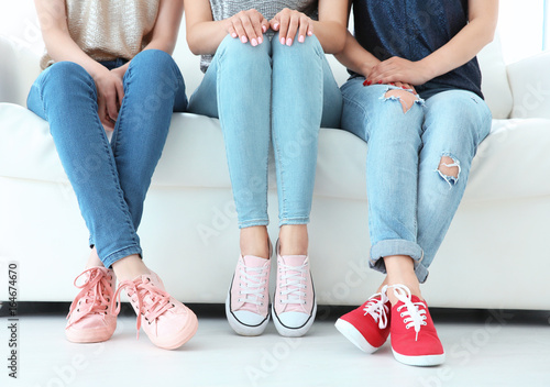 Young women with beautiful legs in jeans and sneakers sitting on sofa