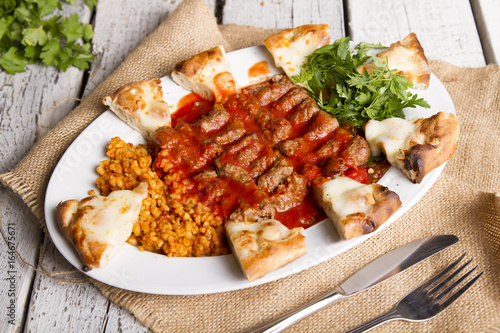 Turkish and Arabic Traditional Ramadan Iskender Adana Kofte Kebab with parsley, bulgur and cheese bread serving on rustic white wood background.