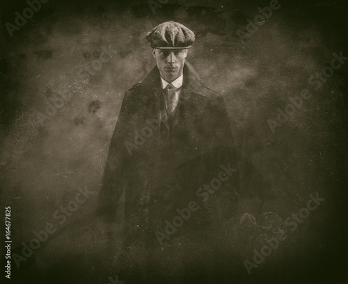 Antique wet plate photo of threatening 1920s english gangster holding gun in smoky room.