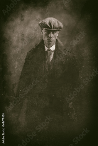 Antique wet plate photo of threatening 1920s english gangster holding gun in smoky room.