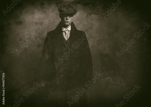 Antique wet plate photo of mysterious 1920s english gangster with flat cap and black coat.