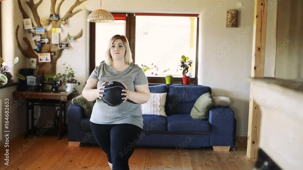 Attractive overweight woman at home working out with medicine ball. Attractive overweight woman at home working out with medicine ball.