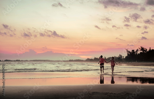 A pair of lovers running along the beach at sunset