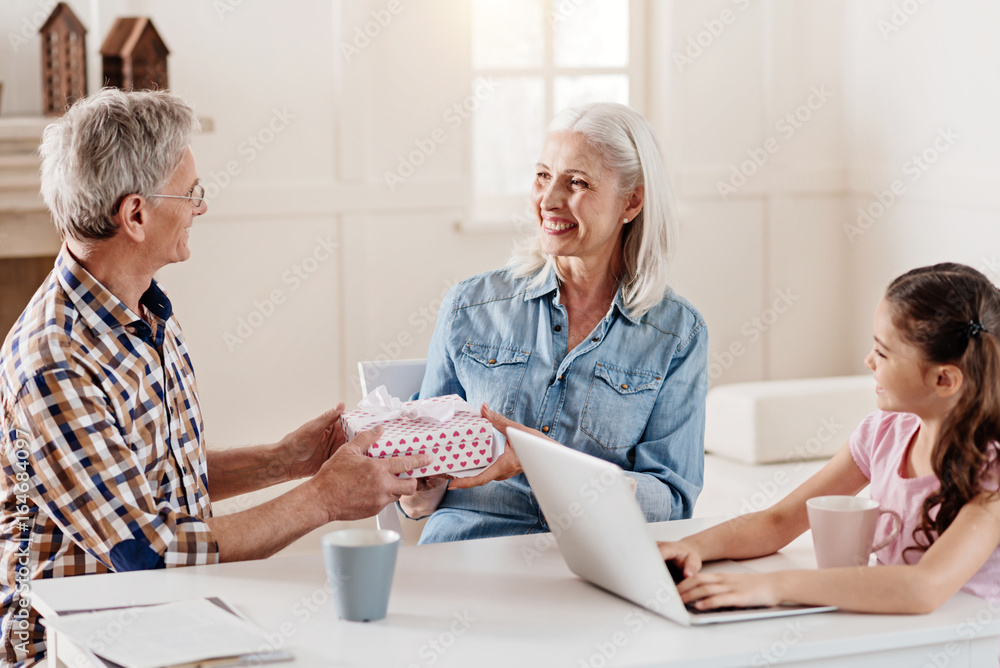Positive delighted grandmother taking gift box from husband Positive delighted grandmother taking gift box from husband