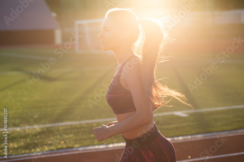 Professional sportswoman running outdoors at sunset. Female athlete in sportswear on stadium outdoors. Workout sport activity.
