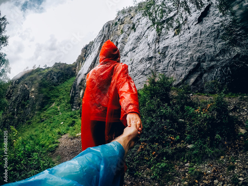 girl in a raincoat in the rain leads the guy to the mountain. Concept follow me to the mountains. photo