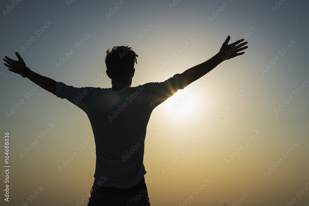 Silhouette of a happy man is strong confidence open arms under the sunset om the top. Freedom and victory concept.