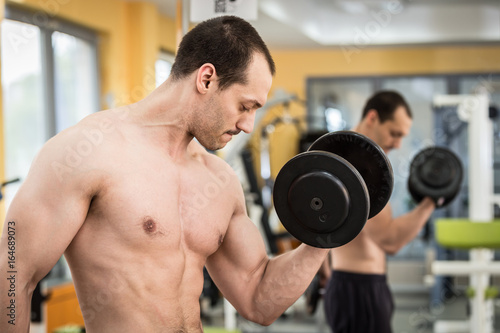 bodybuilder man doing biceps exercise with dumbbell in fitness club