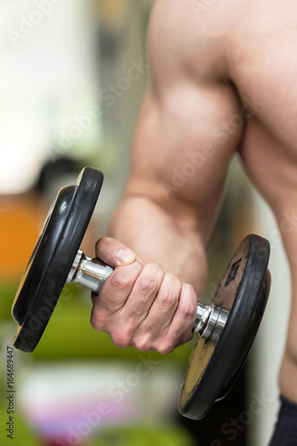 close up photo of bodybuilder man hand doing biceps exercise with dumbbell in fitness club