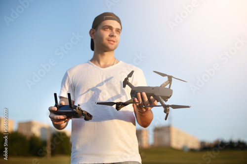 Happy man shows You small compact drone and remote controller. Pilot holds quadcopter and RC in his hands.