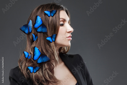 Beauty Fashion Model Girl with a large number of butterflies in hair. Grey background