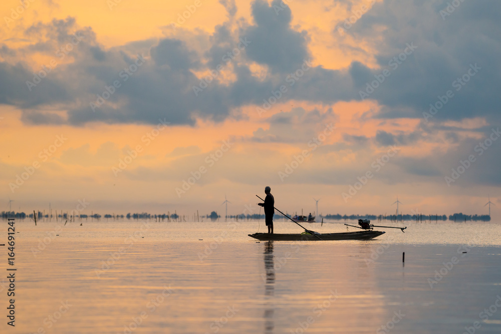 silhouette of fisherman on boat with beautiful sunset sky in  in wetlands Thale Noi, South of THAILAND.