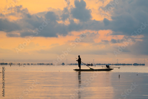 silhouette of fisherman on boat with beautiful sunset sky in in wetlands Thale Noi, South of THAILAND.