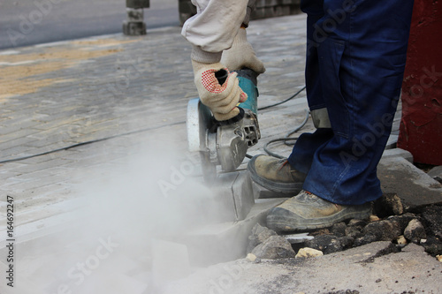 A worker mason cuts a curb with a circular saw when repair of the sidewalk photo