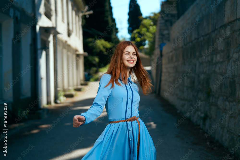 Young beautiful woman in blue dress walking along the boulevard in the city