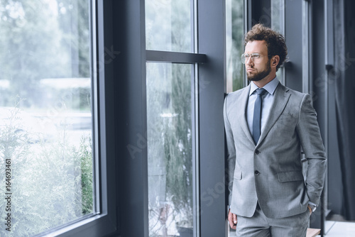 young pensive businessman in suit looking out window in office