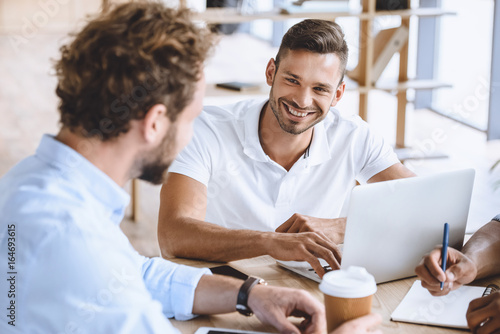 portrait of smiling businessman with laptop on meeting with coworkers in office