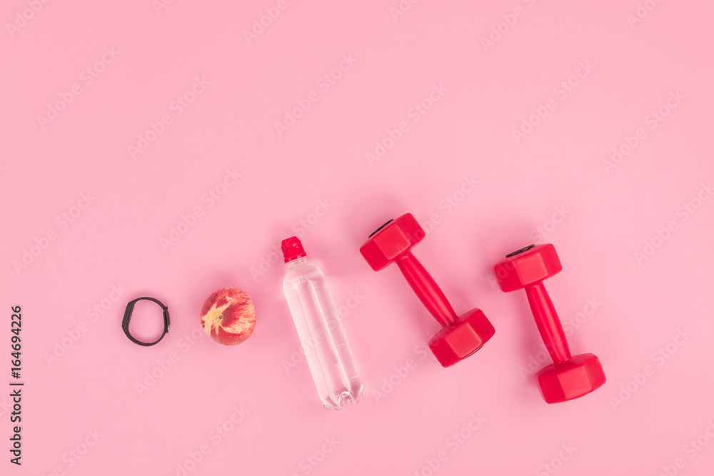 close-up view of fitness tracker, peach, bottle with water and dumbbells isolated on pink