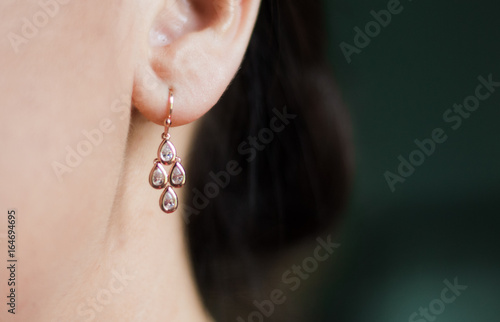 Fototapet Rose gold earring hangs in Caucasian brunette woman's ear