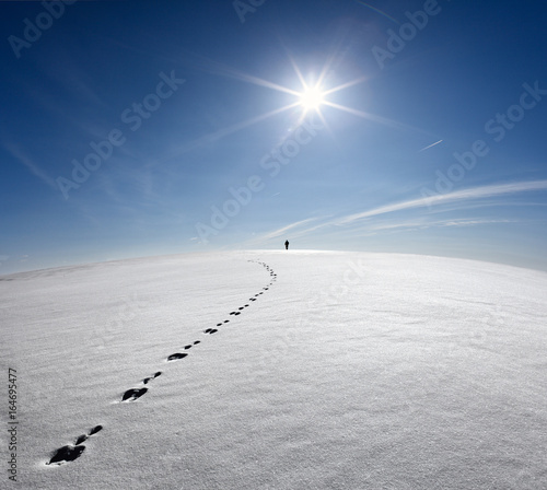 Obraz na płótnie Man,Earth,Universe. Lonely Man Walking On Snow Crust Field On The Trail Of Hare At The Background Of The Sun And Flying Plane. Abstract Photo Silhouette Of A Man On The Road In Winter Empty Field w salonie