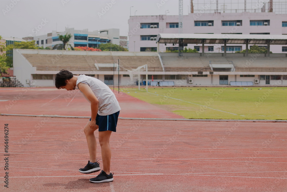 Handsome young Asian runner man warming up before run on track in the stadium