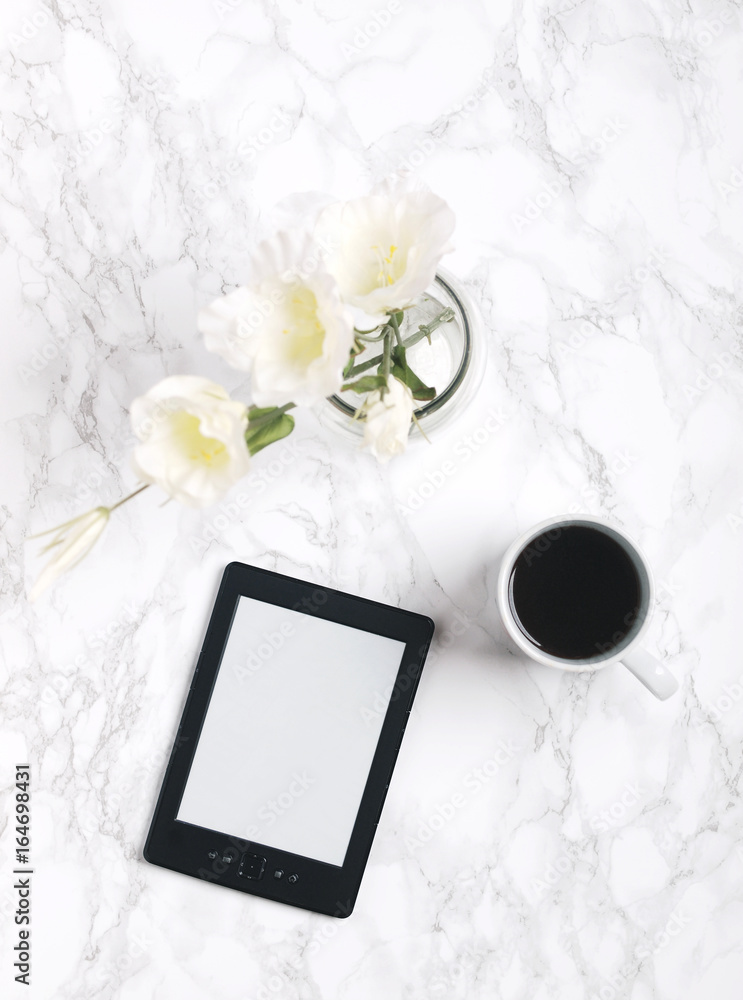 Tablet or e-reader with white flowers and black coffee on white marble background. Flat lay. Top view. Copy space. Tablet or e-reader with white flowers and black coffee on white marble background. Flat lay. Top view. Copy space.