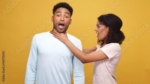 Angry young african woman strangling her boyfriend isolated over yellow background