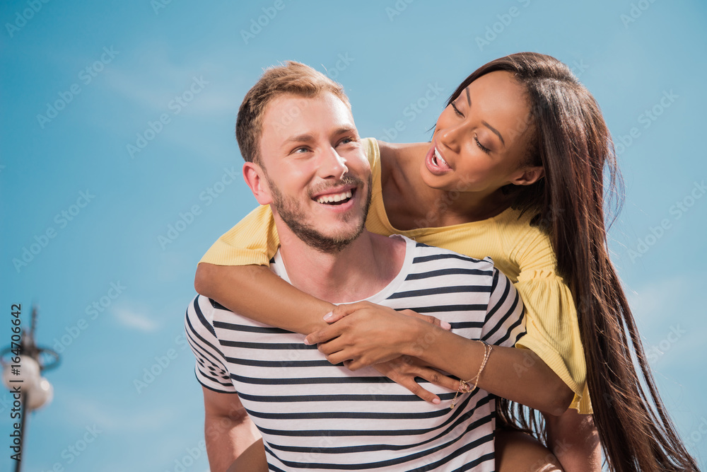 Fototapeta premium Happy young multiethnic couple smiling and piggybacking in city