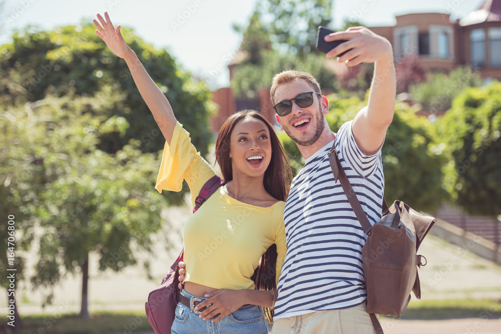 young happy multiethnic couple gesturing and taking selfie on smartphone