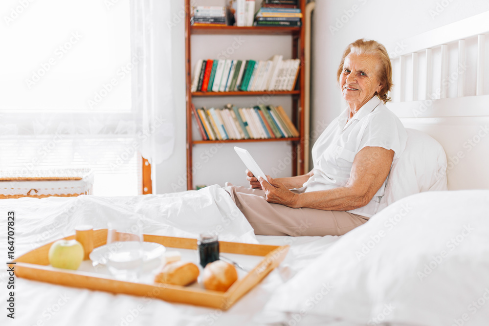 Elderly woman having breakfast in bed whilst using her tablet Elderly woman having breakfast in bed whilst using her tablet