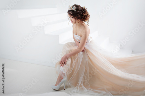 Bride sits on the stairs. Portrait of a beautiful girl in a wedding dress. Dancing Bride, white background. photo