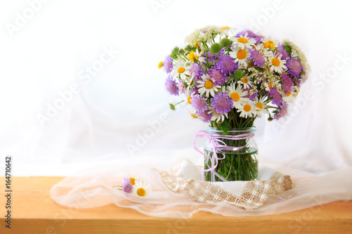 Chamomiles bouquett in vase on fabric background.