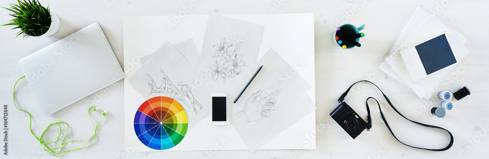 Aerial view of designer desk with creative tools: laptop, camera, film, sketches, phone, etc