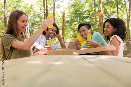 Cheerful young multiethnic friends students outdoors drinking juice eating pizza