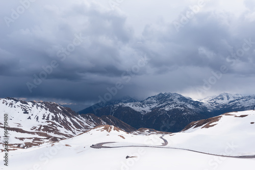 A landscape view from Hochtor tunnel on the Grossglockner high alpine road. Looking towards Heiligenblut in Carinthia with blue sky, mountains clouds and snow and the Grossglockner high alpine road.