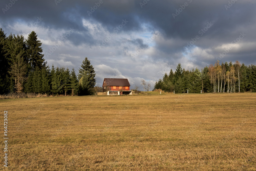 A hunting lodge in the woods with a red roof and storm black dark clouds over it A hunting lodge in the woods with a red roof and storm black dark clouds over it