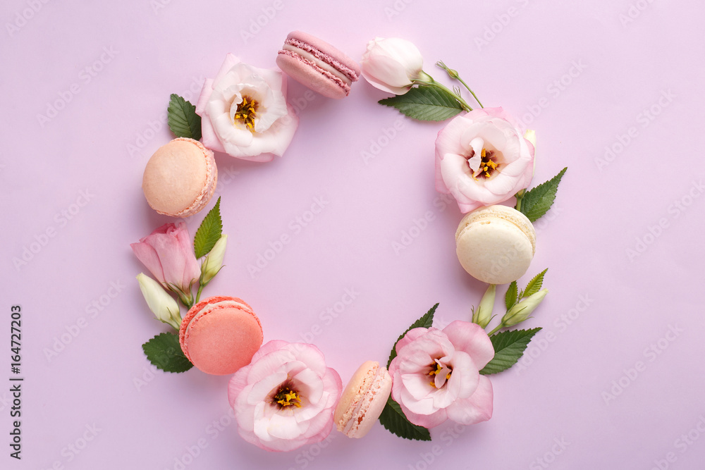 Macarons and flowers wreath on a purple background. Colorful french dessert with fresh flowers. Top view