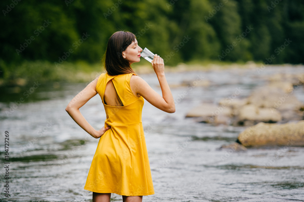 Sexy tanned long haired cutie in yellow dress standing in river